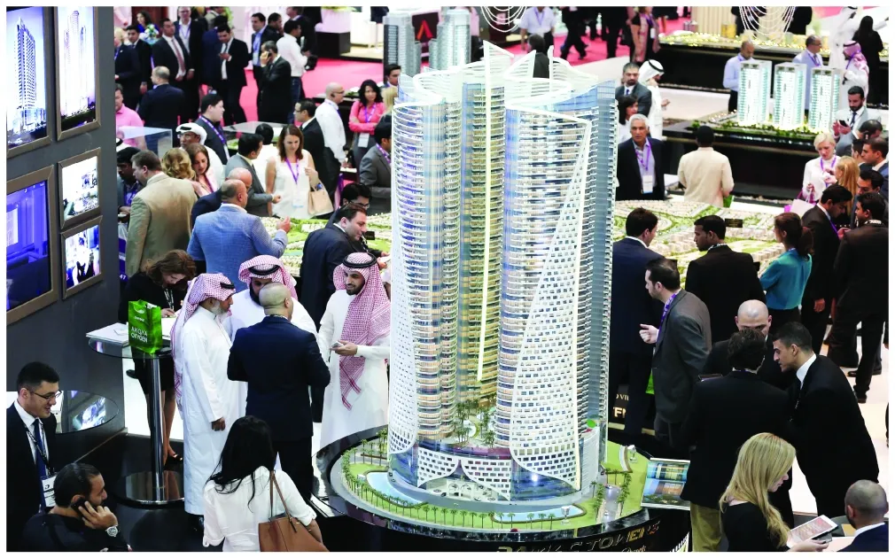 International investors attending a Dubai real estate exhibition with scale model of luxury residential tower.